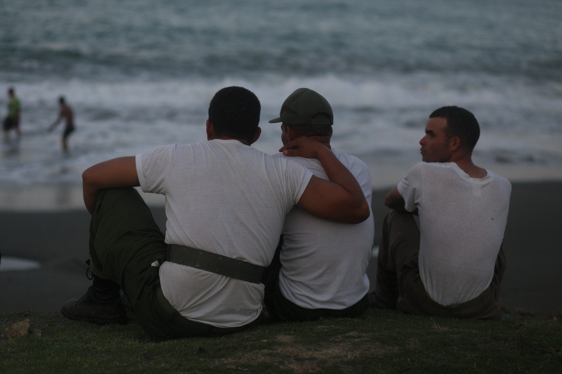 Drei Männer sitzen am Strand und blicken aufs Meer