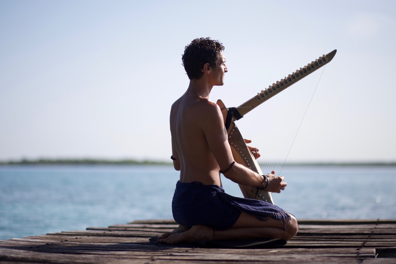 Mann sitzt mit seiner handgebauten Harfe auf dem Steg am See von Bacalar