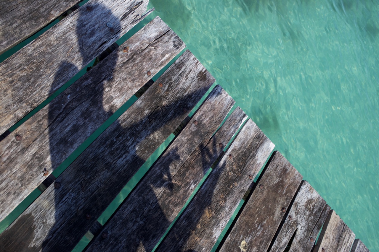 Schatten auf den Holzplanken eines Stegs über türkisem Wasser
