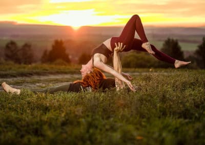 Frau in einer Rückbeuge auf einer Wiese im Sonnenuntergang