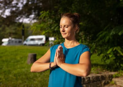 Yoga mit Sandra – Frau in blauem Shirt mit gefalteten Händen auf einer Wiese im Weimarer Land