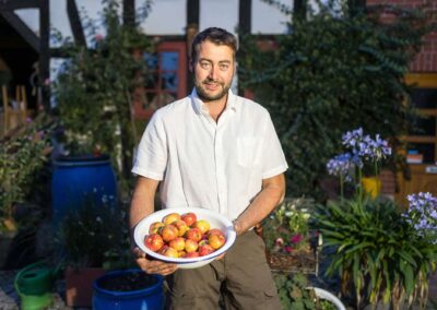 Mann in weißem Hemd hält eine Schale mit Früchten in einem Hofgarten in Kleinromstedt