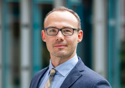 Business-Porträt eines Mannes mit Brille und Krawatte vor Glasfassade
