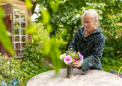 Ältere Frau arrangiert Blumen in einer Vase im grünen Garten