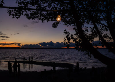 See in der Abenddämmerung mit Silhouetten von Bäumen und Menschen am Ufer